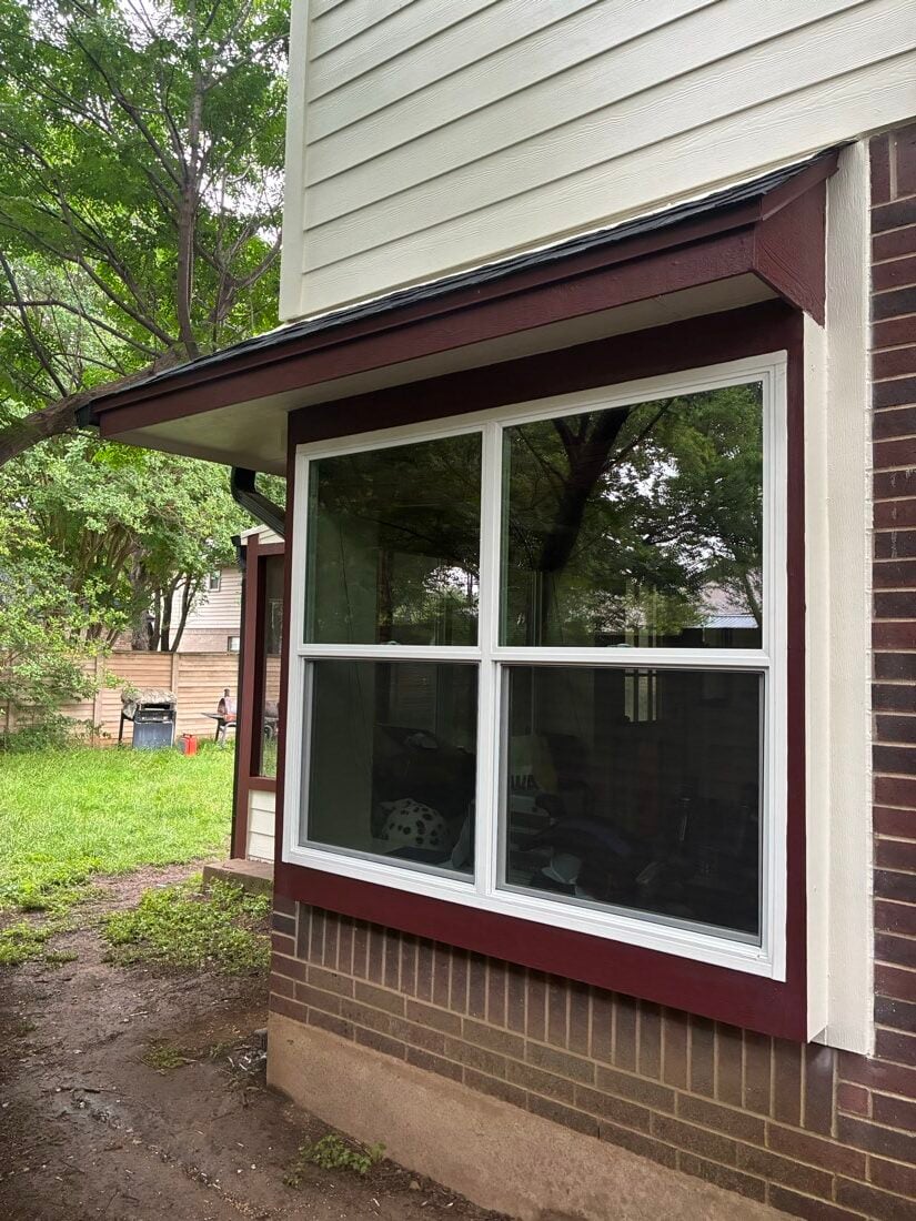 New white double-hung window unit installed with dark red frame trim over brick on an Austin TX home